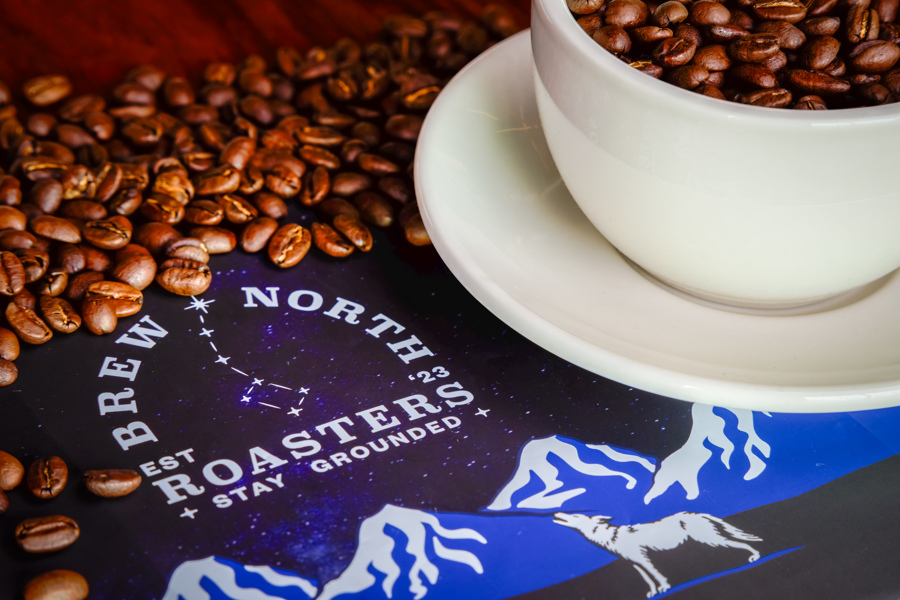 Cup of ethically-sourced coffee beans over Brew North Roasters logo